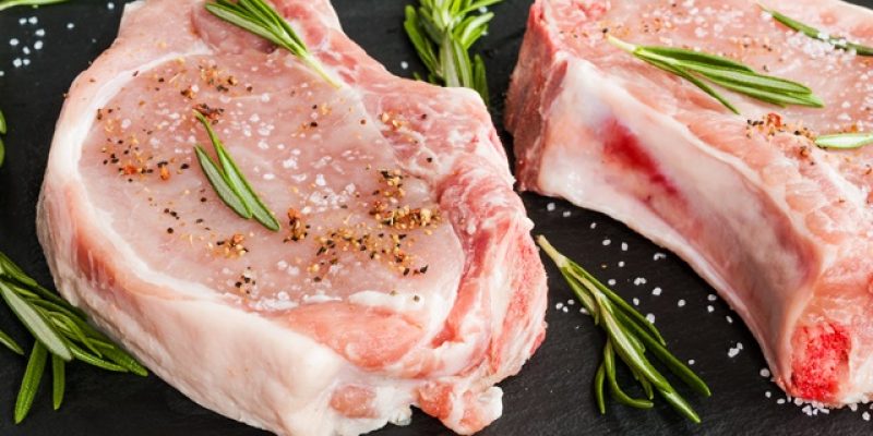 Pork steaks with rosemary on black stone background.